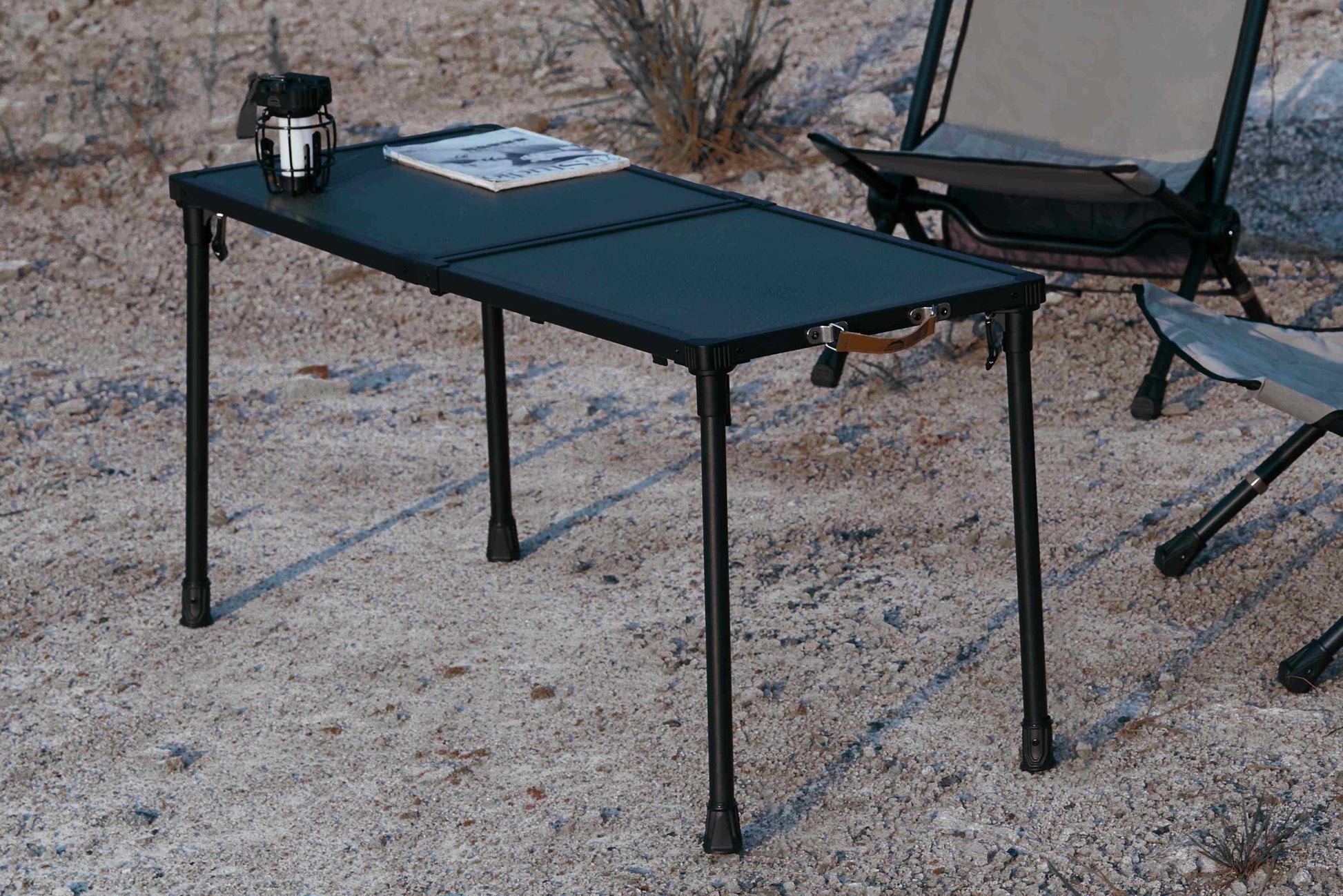 Camping chair and table set up outdoors near a body of water.