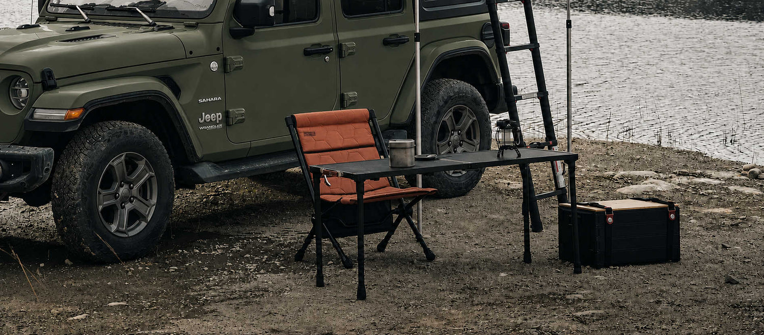 Green Jeep Wrangler with camping gear near a body of water
