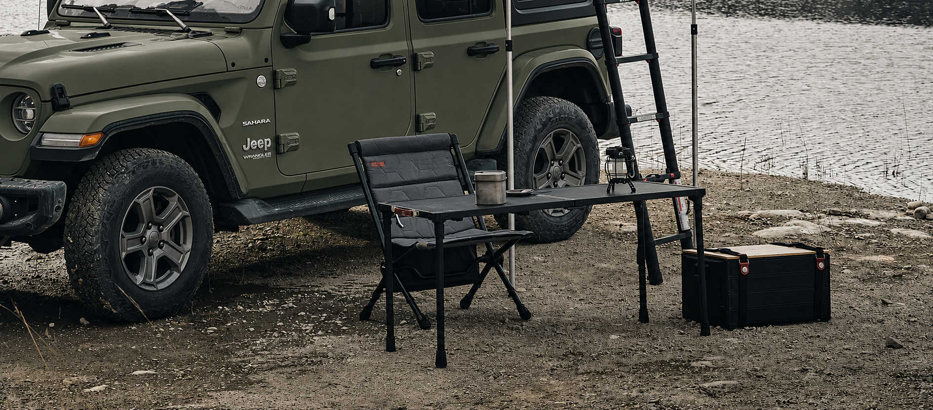 Green Jeep Wrangler with camping gear near a body of water