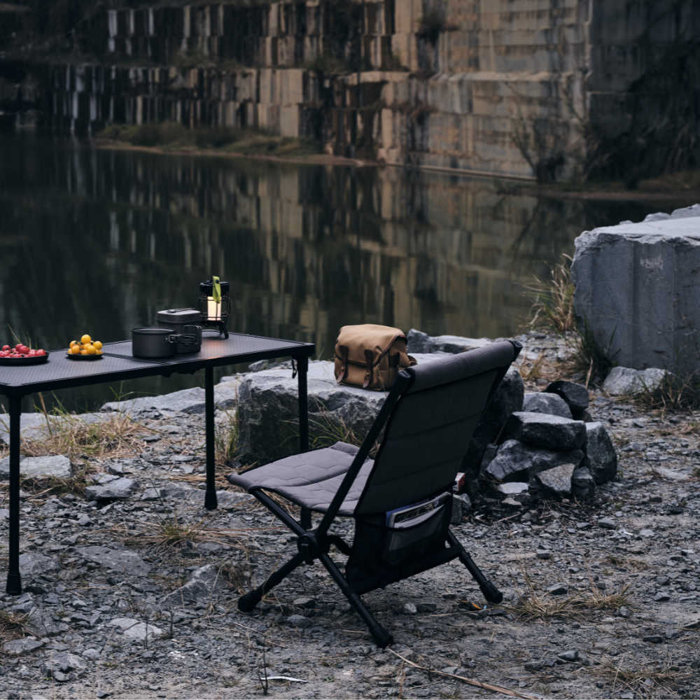 Outdoor setting with a table, chair, and backpack near a body of water.