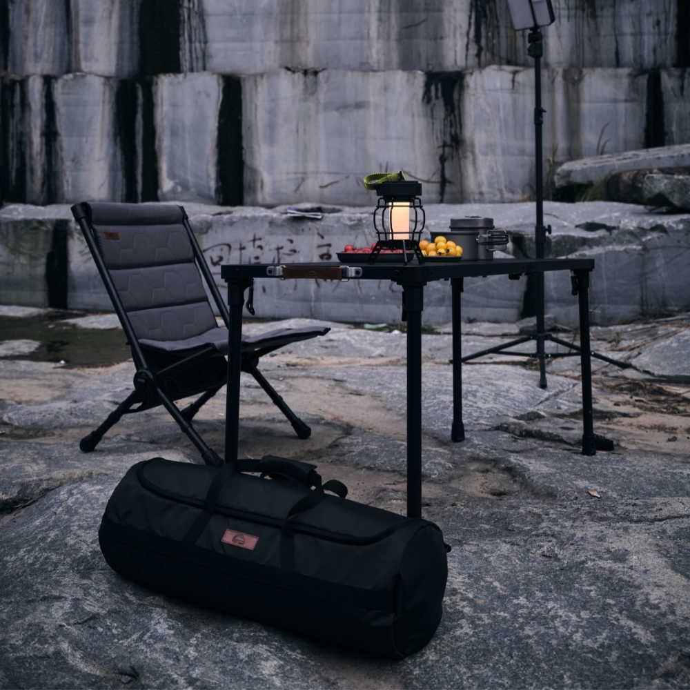 Camping setup with chair, table, lantern, and bag on a rocky surface.
