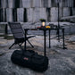 Camping setup with chair, table, lantern, and bag on a rocky surface.