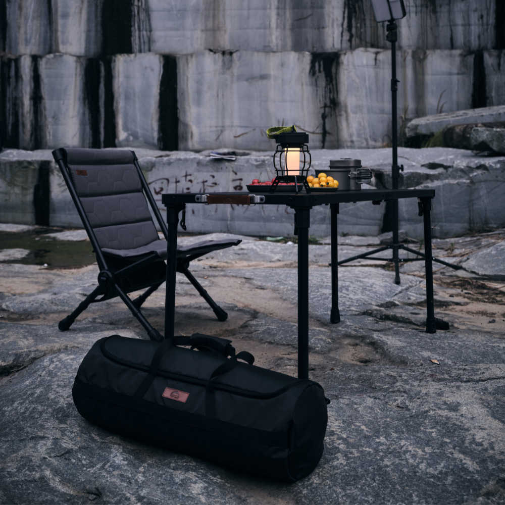 Camping setup with chair, table, lantern, and bag on a rocky surface.