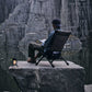 Person sitting on a chair by a rocky cliff with a lantern nearby