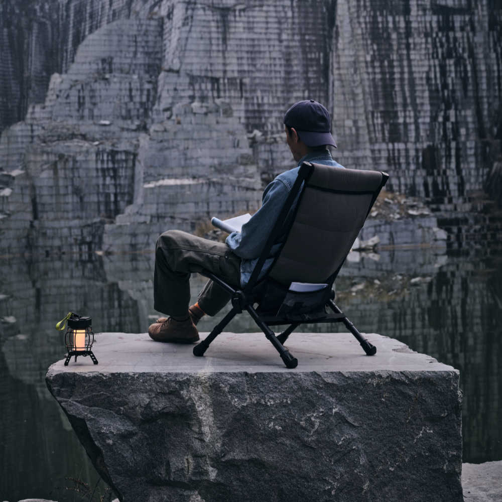 Person sitting on a chair by a rocky cliff with a lantern nearby