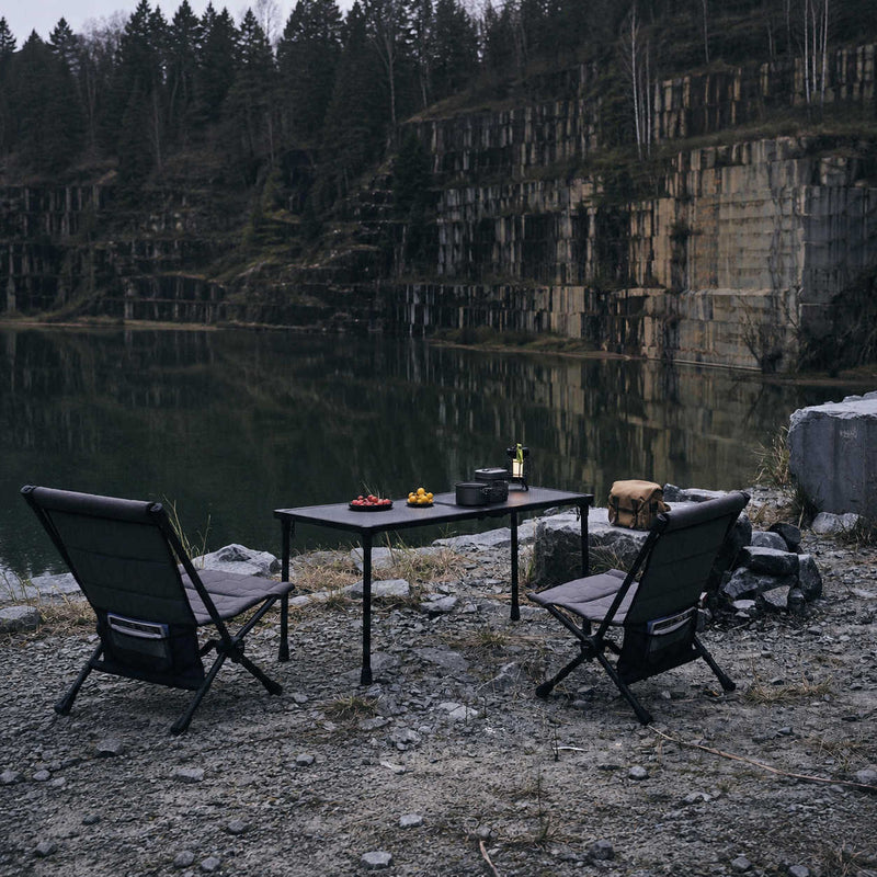 Outdoor setting with a table and chairs by a lake with stone walls.