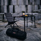 Camping setup with chair, table, lantern, and duffel bag against a rocky background