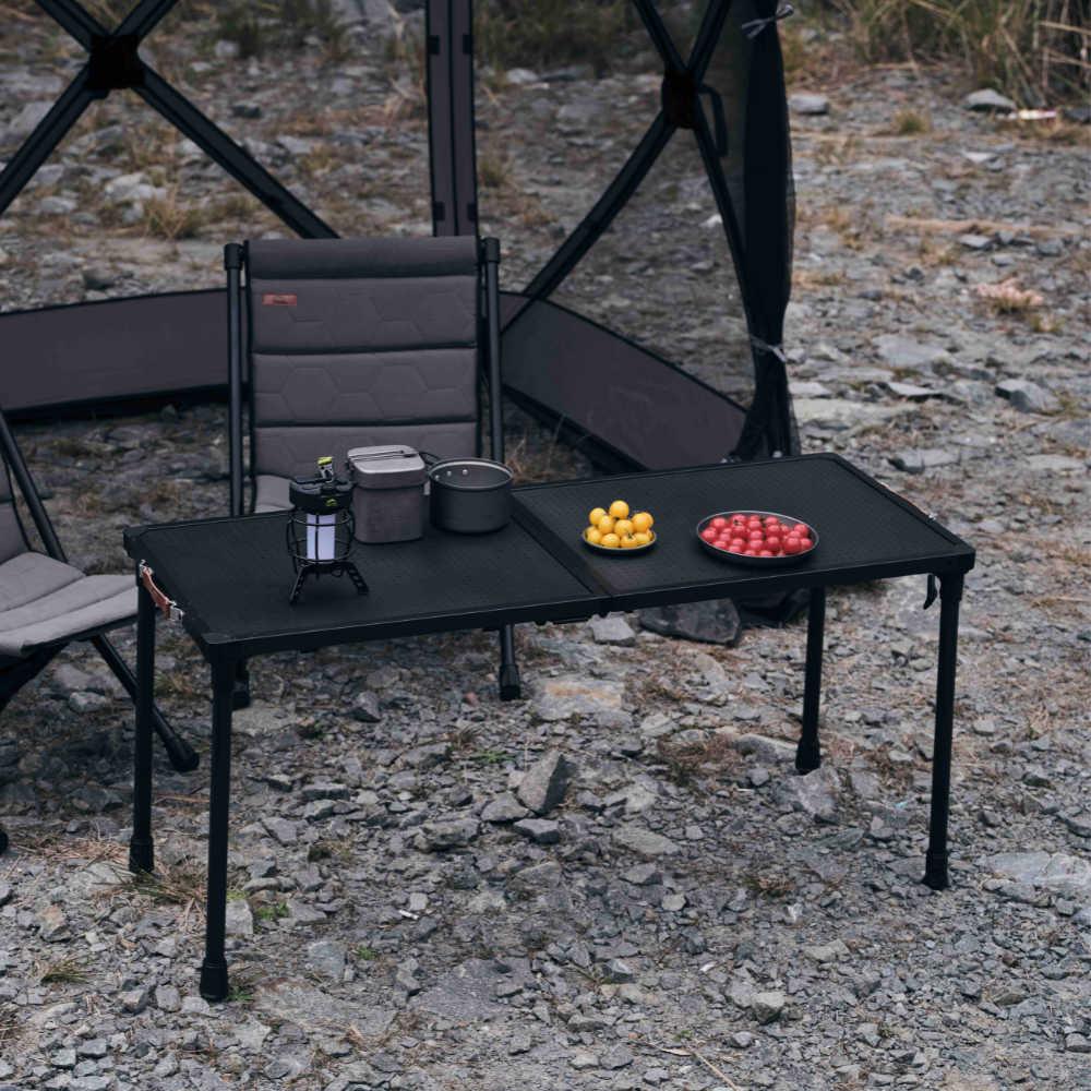 Black camping table with chairs and food items on a rocky ground