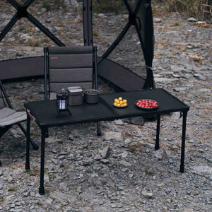 Black camping table with chairs and food items on a rocky ground