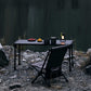 Black table and chair set by a body of water with snacks and a lantern.