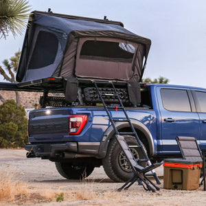 Desert cruiser rooftop tent mounted on the roof of a blue truck, with an outdoor setting in the background.