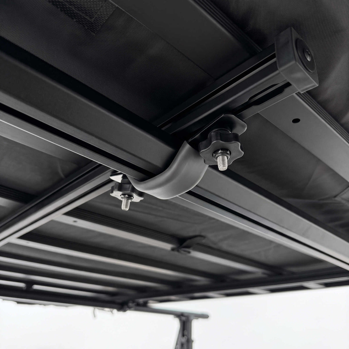Close-up of a black retractable tent or canopy mounted on a metal frame, showing the track system, bracket, and attachment hardware.