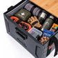 An open black outdoor storage box with a wood-grain lid, filled with camping gear.  The box has a visible logo on the front and side.