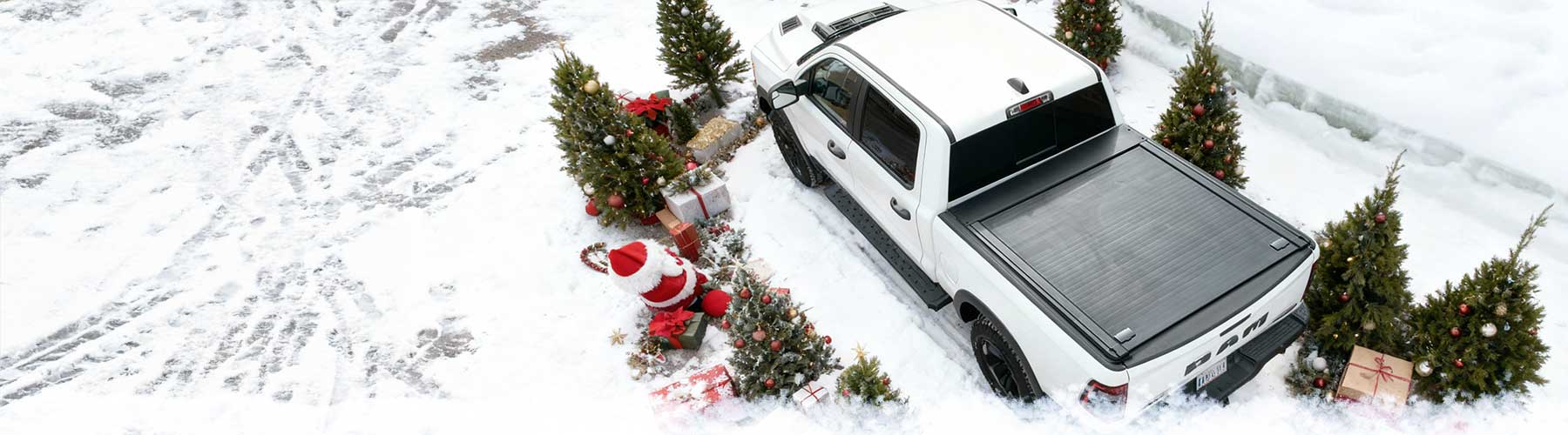 White truck with a black tonneau cover parked in a snowy landscape with Christmas trees and decorations.