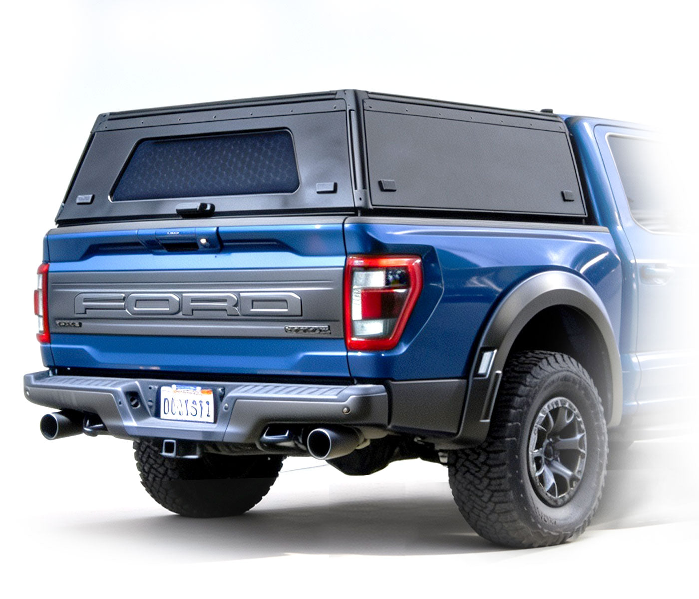 Black truck bed rack system with side panels and a frame, shown disassembled in front of a faded tan pickup truck. Blue and orange 'FLEX MOD CAP CAP RACK' logo appears in the upper left on a white background.