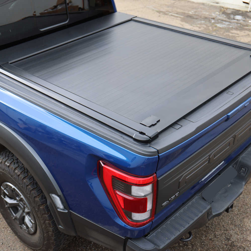 Close-up of a blue truck with a black tonneau cover on a gravel surface